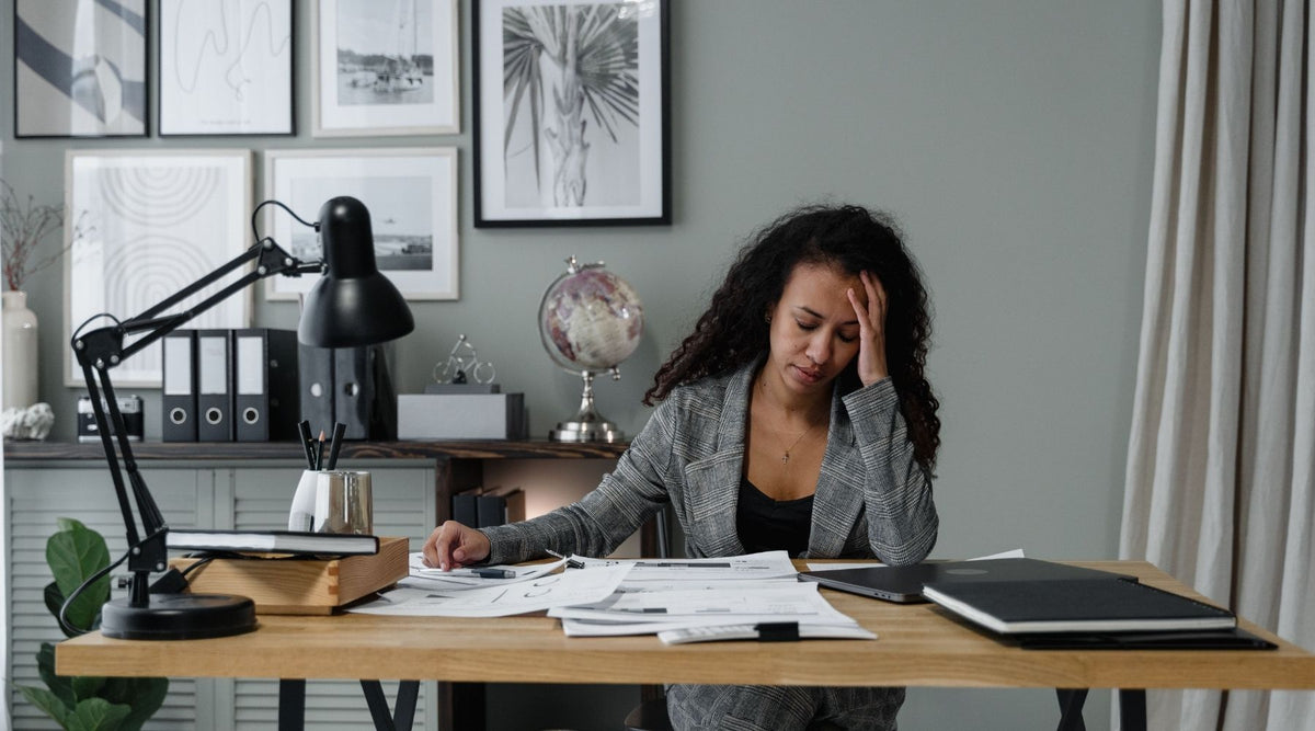 woman at desk, leaning forehead on one hand